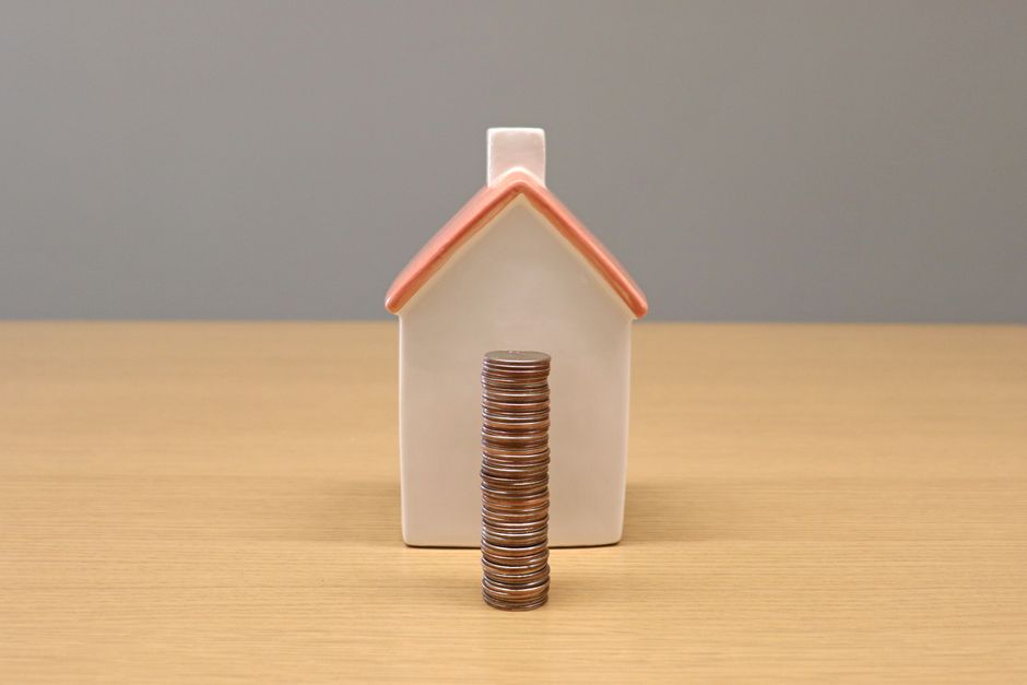A conceptual still life image of stacked coins in front of a porcelain house, symbolizing savings and investment.