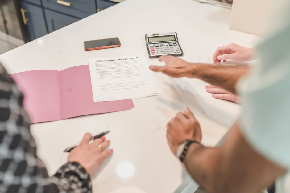 Hands gesturing during a real estate document review on a modern office desk with a calculator.
