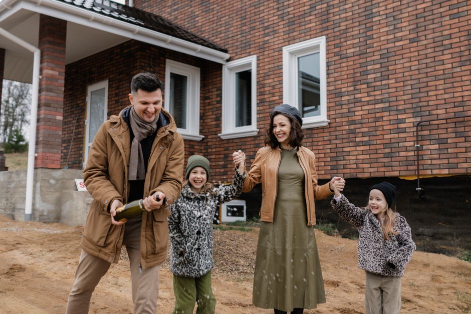 A family joyfully celebrates outside their newly purchased brick house with champagne.